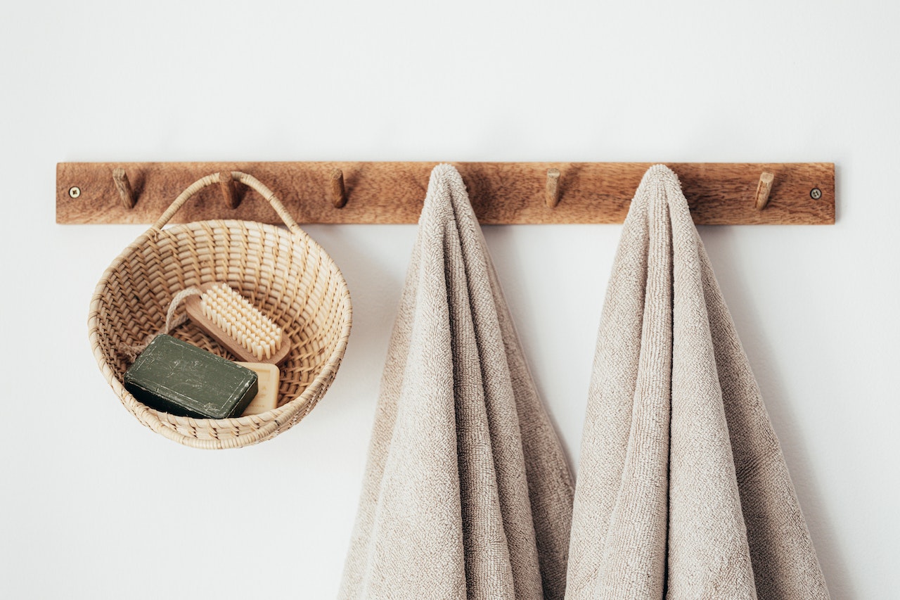 wooden wall rack with wooden basket with bar soaps, and two towels hanging from its pins